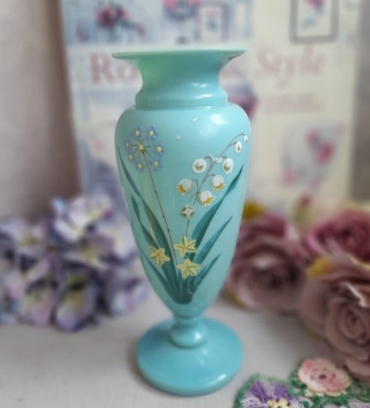 Turquoise vase with floral design in front of blurred flowers