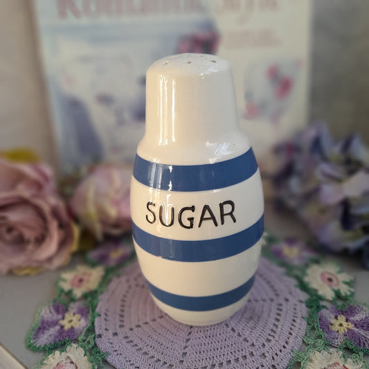Decorative sugar container with blue stripes on a floral surface